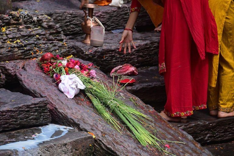 Holy grass kusha laid out on a stone with flowers. Two women are standing next to the stone - their faces are not visible.