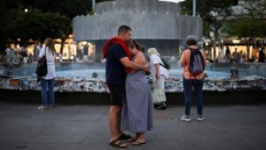 A man and woman embrace in front of the fountain at Dizengoff Square. The woman has her hand to her eyes as if she is crying.
