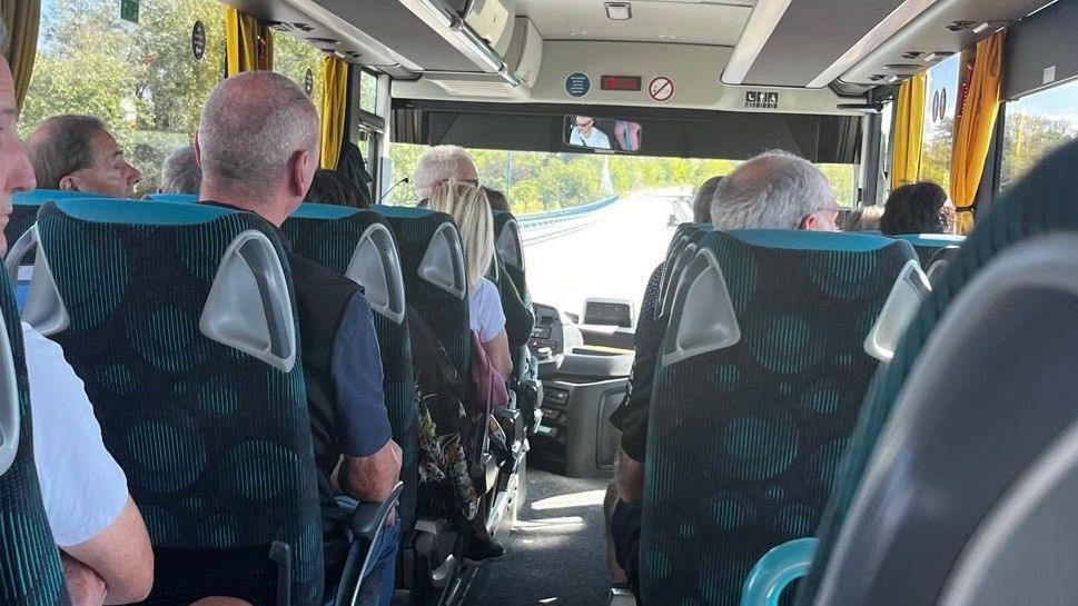 A photo showing the inside of a coach, and the backs of passengers' heads as they sit in their seats. Some are looking out the window.