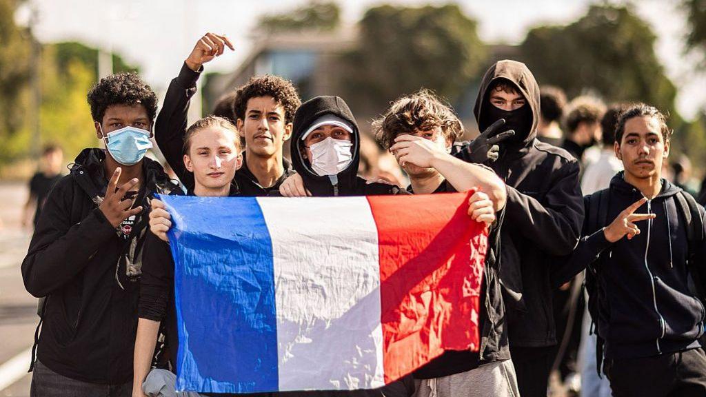 A group of protesters carrying French flags posing in front of law enforcement officers outside the Lycee Maillol in Perpignan, in the Pyrenees-Orientales department in southern France, on October 6, 2026.